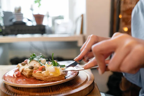 연어, 양상추 잎, 데친 달걀을 곁들인 벨기에 전통 와플. 한 젊은 여성이 카페에서 아침 식사를 하고, 포크와 칼을 들고 있는. — 스톡 사진