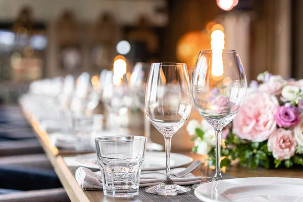 Şarap bardakları ön planda. Düğün Ziyafeti ya da gala yemeği. Misafirler için sandalye ve masa, çatal bıçak takımı ve tabak ile servis.