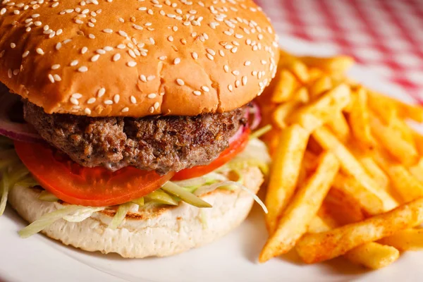 Sabrosa hamburguesa en el restaurante. Pan de sésamo, carne Patty, tomate, lechuga y pepinillo. Servido con papas fritas — Foto de Stock