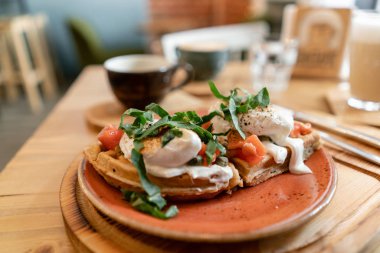 Somon, marul yaprakları ve haşlanmış yumurta ile geleneksel Belçika waffle. Genç bir kadın bir kafede kahvaltı yapıyor, elinde çatal ve bıçak yakın çekim.