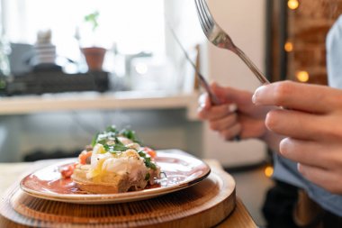 Somon, marul yaprakları ve haşlanmış yumurta ile geleneksel Belçika waffle. Genç bir kadın bir kafede kahvaltı yapıyor, elinde çatal ve bıçak yakın çekim.
