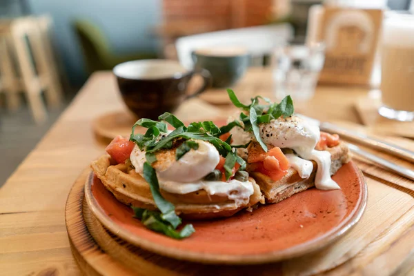 Somon, marul yaprakları ve haşlanmış yumurta ile geleneksel Belçika waffle. Genç bir kadın bir kafede kahvaltı yapıyor, elinde çatal ve bıçak yakın çekim.