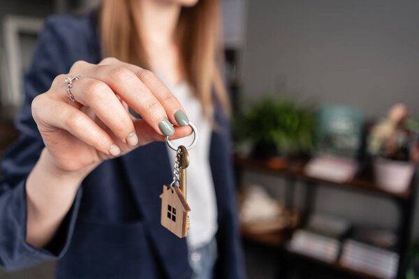In the foreground house key in womans hands. Young pretty woman. Modern light lobby interior. Real estate, hypothec, moving home or renting property.
