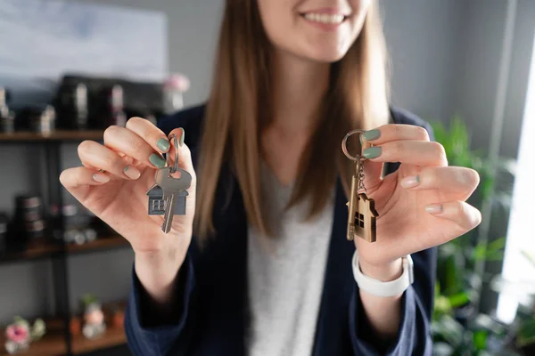 two house keys in womans hands. Young pretty woman smiles. Modern light lobby interior. Real estate, hypothec, moving home or renting property.