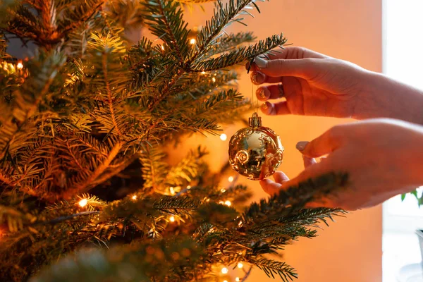 Winter vakantie in een huis interieur. Gelukkig jonge vrouw versieren kerstboom thuis. Gouden en witte kerst speelgoed, lichten slingers. Natuurlijk Deens sparrenhout — Stockfoto