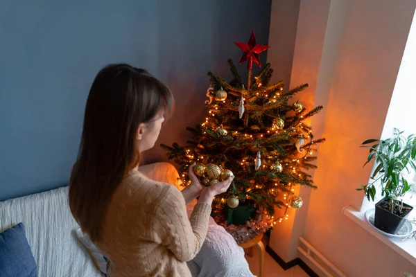 Gelukkig jonge vrouw versieren kerstboom thuis. Winter vakantie in een huis interieur. Gouden en witte kerst speelgoed, lichten slingers. Natuurlijk Deens sparrenhout — Stockfoto