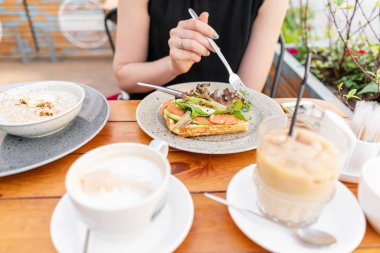 Somon, marul yaprakları ve haşlanmış yumurta ile geleneksel Belçikalı Waffle. Genç bir kadın bir yaz kafede kahvaltı yapıyor, bir çatal ve bir bıçak yakın çekim ile eller. Buz küpleri ile soğuk kahve