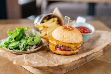 Marul, domates, patates kızartması ve eritilmiş peynirile çizburger. Restorandaki masa. Sağlıksız gıda.