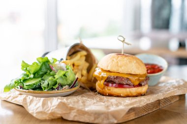 Marul, domates, patates kızartması ve eritilmiş peynirile çizburger. Restorandaki masa. Sağlıksız gıda.