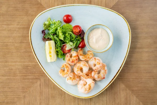 Délicieuses crevettes fraîches aux légumes frais et au citron vert. Assiette sur table en bois. Sauce à la crème — Photo