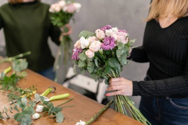 Close-up flowers in hand. Florist workplace. Woman arranging a bouquet with roses, carnation and other flowers. A teacher of floristry in master classes or courses clipart