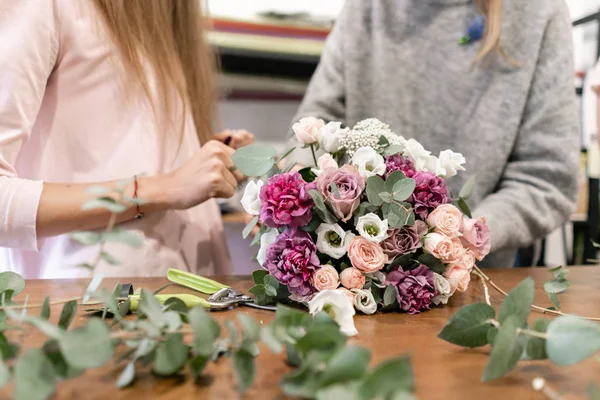 Close-up flowers in hand. Florist workplace. Woman arranging a bouquet with roses, carnation and other flowers. A teacher of floristry in master classes or courses — Stock Photo, Image