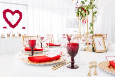 Masa ayarı kırmızı peçeteler ve gözlükler, altın tabaklar. Misafirler için hazır bir düğün çadır dekorasyonu Iç. Dekor çiçekleri. Kırmızı tema