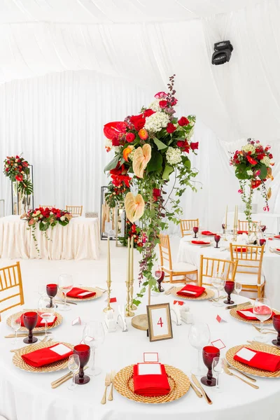 Beautiful banquet hall under a tent for a wedding reception. Interior of a wedding tent decoration ready for guests. Decor flowers. Red theme