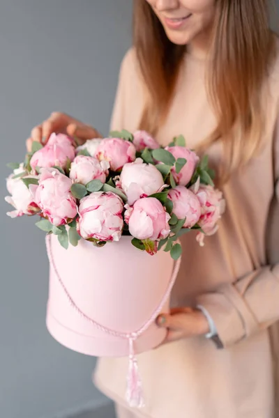 Pink peonies in pink round box. Beautiful peony flower in womans hands for catalog or online store. Floral shop concept. Flowers delivery