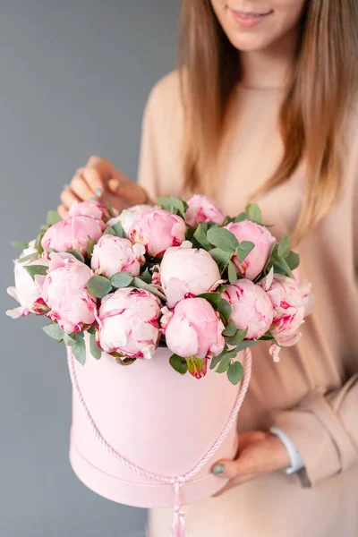 Peônias cor-de-rosa em caixa redonda rosa. Bela flor de peônia em mãos de mulheres de catálogo ou loja online. Conceito de loja floral. Entrega de flores — Fotografia de Stock