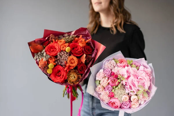 Dos hermosos ramos de flores mixtas en manos de mujeres. el trabajo de la floristería en una florería. Flor recién cortada. Color rojo y rosa — Foto de Stock