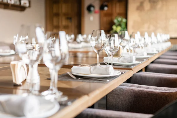 Copos de vinho em primeiro plano. Banquete de casamento ou jantar de gala. As cadeiras e mesa para os hóspedes, servidos com talheres e louças . — Fotografia de Stock