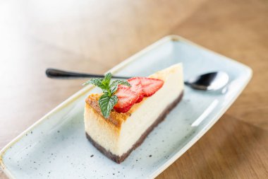Beyaz tabakta çilek ve nane yaprakları ile lezzetli cheesecake Parçası.