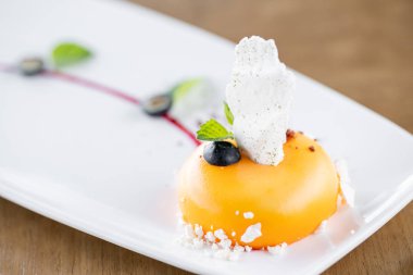 Sarı mus-kek. Fransız tatlısı, yaban mersini, nane ve beyaz tabakta bir parça beze. Şık bir şekilde dekore edilmiştir. Restoran menüsü