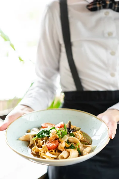 El camarero sostiene un plato de pasta italiana tagliatelle con mariscos y salsa de tomate. Pasta Gamberini. Menú restaurante — Foto de Stock