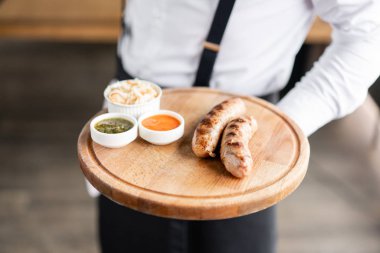 Garson ızgara sosisile tabak tutuyor. Tahta bir tahtada hizmet veriyor. Barbekü restoran menüsü, farklı etfotoğrafları bir dizi. Lahana turşusu ve iki sos