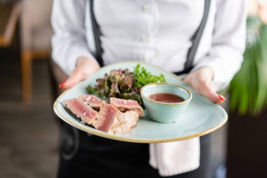 Garson marul ve acı sos lu orta nadir ton balığı tutuyor. Restoran menüsü