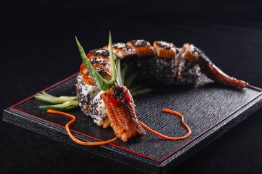 Suşi Ejder yılan balığı, salatalık ve avokado siyah bir arka plan ile. Japon yemekleri, lezzetli yemek öğle yemeği için