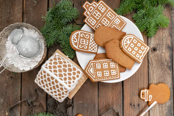 O mulțime de biscuiți de ghimbir sub formă de case europene pe masă de lemn maro. Decorat cu glazură dulce albă. Starea de spirit de Crăciun, dimineața de iarnă . — Fotografie, imagine de stoc