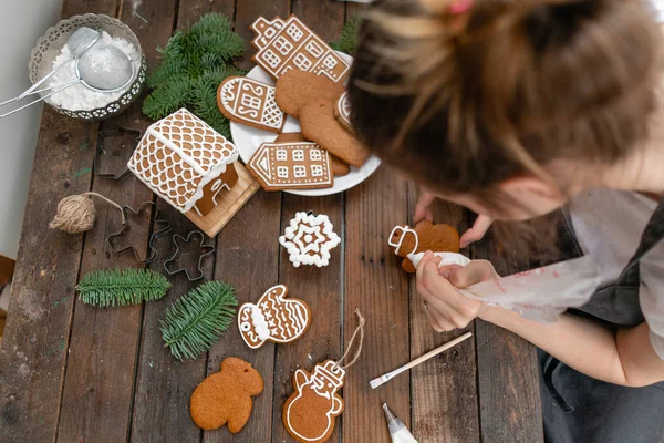 Helado de panadería navideña. Mujer decorando galletas de miel de jengibre sobre mesa marrón de madera. Primer plano, espacio de copia. Galleta en blanco casa de jengibre, listo para decorar . — Foto de Stock