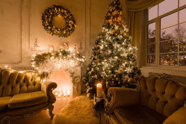 Noel akşam mum ışığında. Klasik dairelerde beyaz bir şömine, dekore edilmiş ağaç, kanepe, büyük pencereler ve avize.