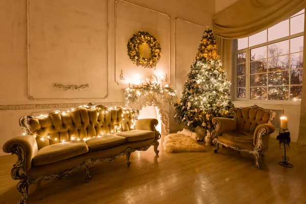 Christmas evening by candlelight. classic apartments with a white fireplace, decorated tree, sofa, large windows and chandelier. — Stock Photo, Image