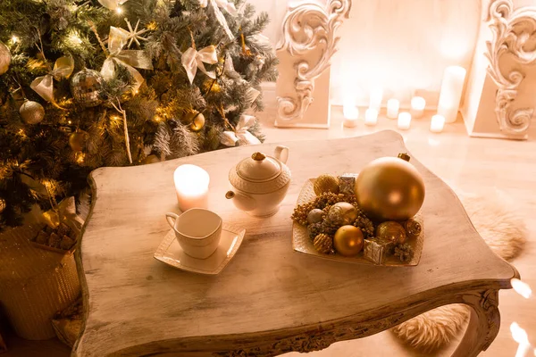 Tea time, white teapot and cups on the table. Decorated Christmas tree. Classic apartments with a white fireplace. — Stock Photo, Image