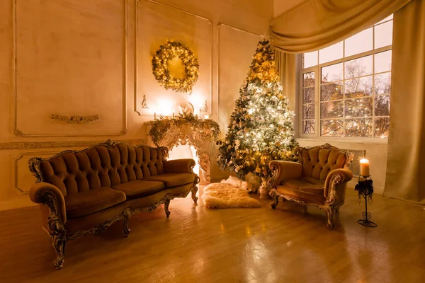 Christmas evening by candlelight. classic apartments with a white fireplace, decorated tree, sofa, large windows and chandelier. — Stock Photo, Image