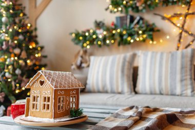 Parlak oturma odasında Noel sabahı. Noel için dekore edilmiş arka plandaki ev yapımı zencefilli kurabiye evi..