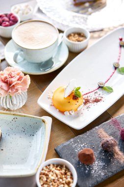 Sarı köpüklü kek. Kafede kahvaltı, sabah kahvesi. Kapuçino ve masada bir sürü tatlı var. Fransız tatlısı, yabanmersini, nane şekeri ve beyaz tabakta bir parça krema. Restoran menüsü