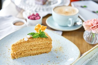 Kremalı ve nane yaprağıyla süslenmiş bal süngeri pastası kafede kahvaltı, sabah kahvesi. Cappuccino ve masada bir sürü tatlı..