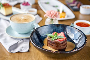 Çikolatalı kek, karamel, çilek ve nane yaprağı ile süslenmiş. Kafede kahvaltı, sabah kahvesi. Cappuccino ve masada bir sürü tatlı..