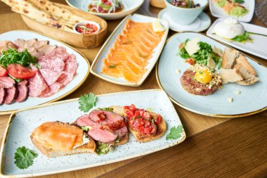 Biftekli, domatesli ve somonlu Tabakların çeşitleri masada. Masada çeşitli abur cuburlar ve antipastalar var. Restoran menüsü. İtalyan mutfağı