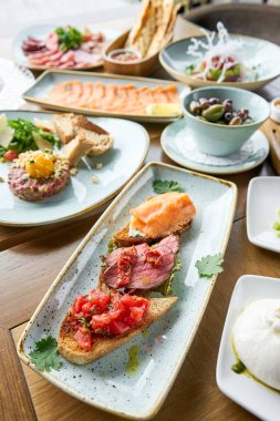 Biftekli, domatesli ve somonlu Tabakların çeşitleri masada. Masada çeşitli abur cuburlar ve antipastalar var. Restoran menüsü. İtalyan mutfağı