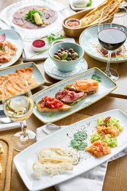 Biftekli, domatesli ve somonlu Tabakların çeşitleri masada. Masada çeşitli abur cuburlar ve antipastalar var. Restoran menüsü. İtalyan mutfağı