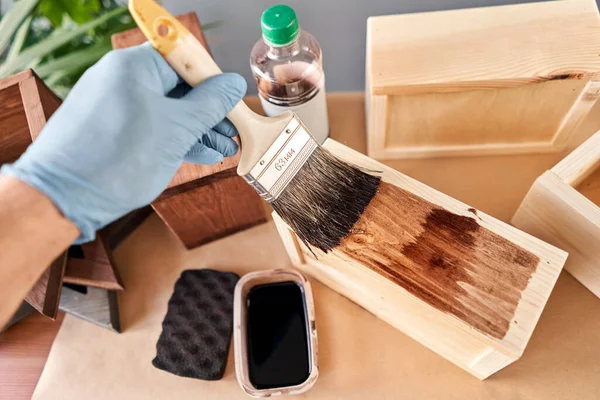 Hombre carpintero barnizado caja de madera para flores con pincel en su taller de carpintería pequeña empresa. En su trabajo, ¿utiliza manchas o conservantes de madera para mostrar el patrón de madera . — Foto de Stock