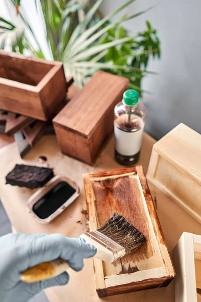 Man timmerman vernis houten krat voor bloemen met borstel in haar kleine bedrijf houtwerk workshop. Gebruik je in je werk vlekken of houtconserveringsmiddelen om het houtpatroon weer te geven?. — Stockfoto