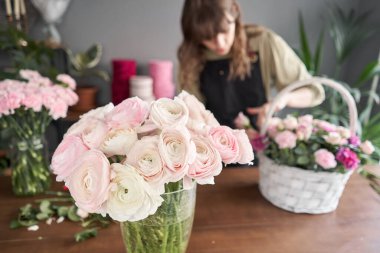 Ranunculus ön plandaki vazoda. Çiçek dükkanı konsepti. Çiçekçi kadın sepette çiçek aranjmanı yapıyor. Güzel bir buket karışık çiçek. Çiçek teslimatı.