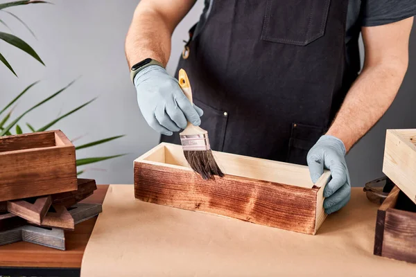 Man carpenter varnishing wooden crate for flowers with brush in her small business woodwork workshop. In your work, do you use stains or wood preservatives to show the wood pattern. — Stock Photo, Image