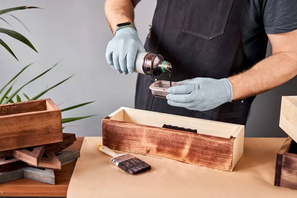 Hombre carpintero barnizado caja de madera para flores con pincel en su taller de carpintería pequeña empresa. En su trabajo, ¿utiliza manchas o conservantes de madera para mostrar el patrón de madera . — Foto de Stock