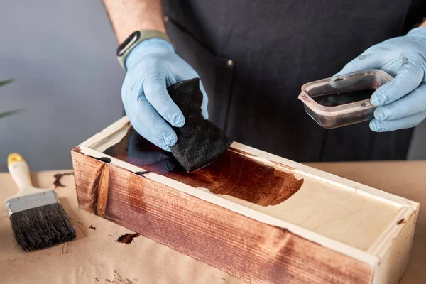 Hombre carpintero barnizado caja de madera para flores con pincel en su taller de carpintería pequeña empresa. En su trabajo, ¿utiliza manchas o conservantes de madera para mostrar el patrón de madera . — Foto de Stock