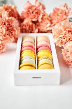 Çiçeklerin arka planında çiçekler olan bir kutuda makarna. Makarna kekleri ve farklı çiçeklerle dolu bir hayat.