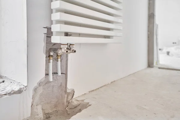 Σύνδεση σωλήνες θέρμανσης σε λευκό καλοριφέρ σε ένα νέο διαμέρισμα υπό κατασκευή. Εργασία ως υδραυλικός, τοποθέτηση καλοριφέρ θέρμανσης νερού στο λευκό τοίχο σε εσωτερικούς χώρους — Φωτογραφία Αρχείου