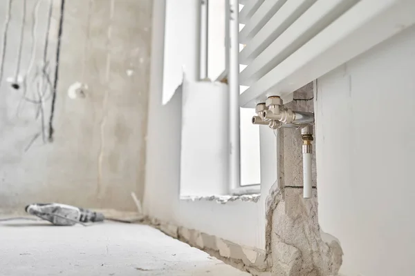 Conexión de tuberías de calefacción a radiador blanco en un nuevo apartamento en construcción. Trabaje como fontanero, montando radiador de calentamiento de agua en la pared blanca en el interior — Foto de Stock